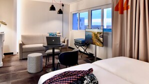 Habitación de hotel con cama, escritorio con una computadora portátil, silla, sofá, televisor y ventana con cortinas.