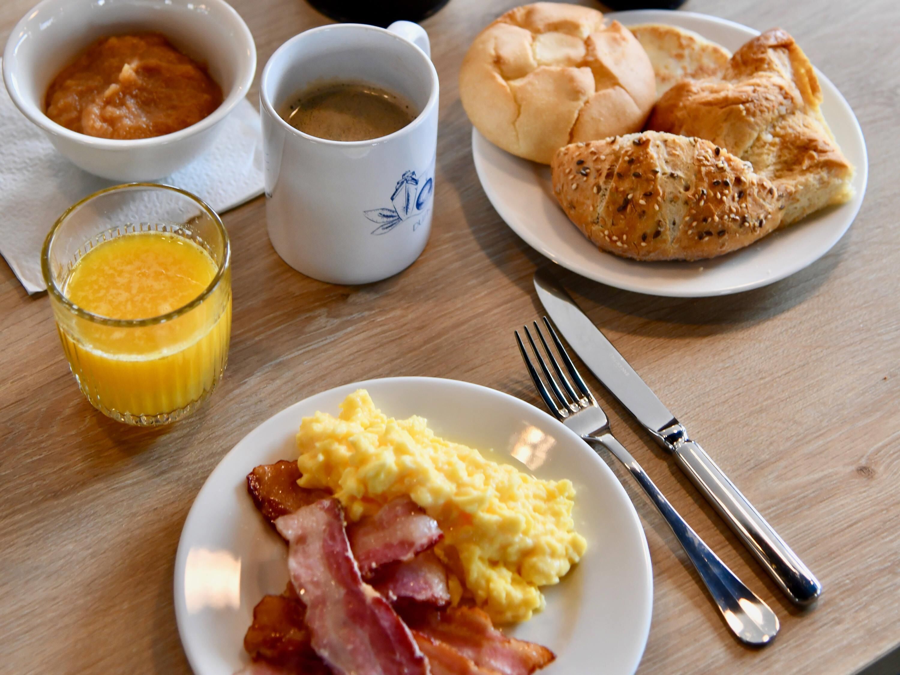 A breakfast plate with scrambled eggs, bacon, toast, and a glass of orange juice.
