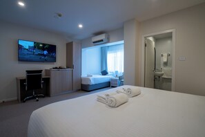 Een hotelkamer met een groot bed, een bureau, een stoel, een televisie, een raam met gordijnen, een badkamer en een airconditioning.