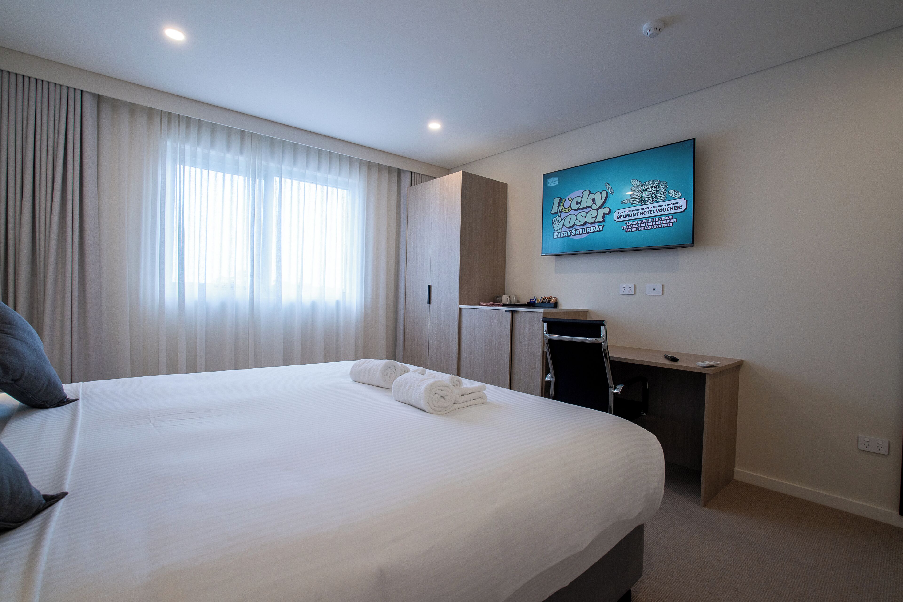 A hotel room with a large bed, a desk, a television, and a window with curtains.