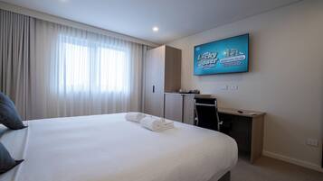 A hotel room with a large bed, a desk, a television, and a window with curtains.