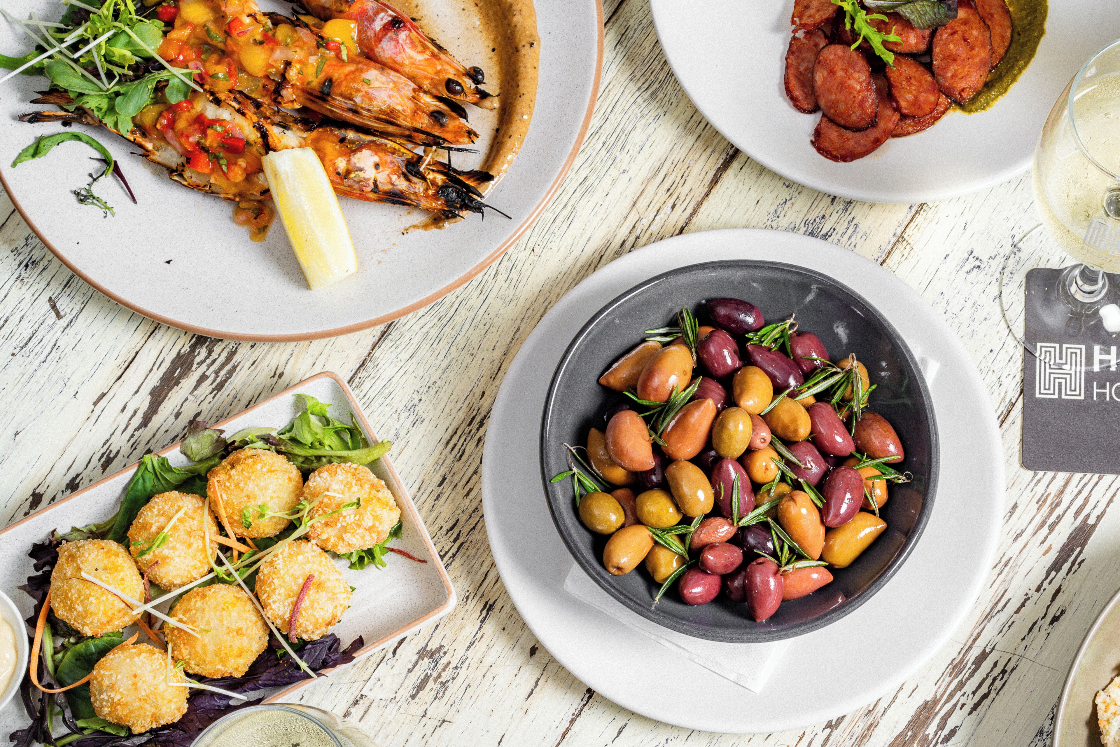 A table with various dishes including grilled shrimp, olives, and bread rolls.
