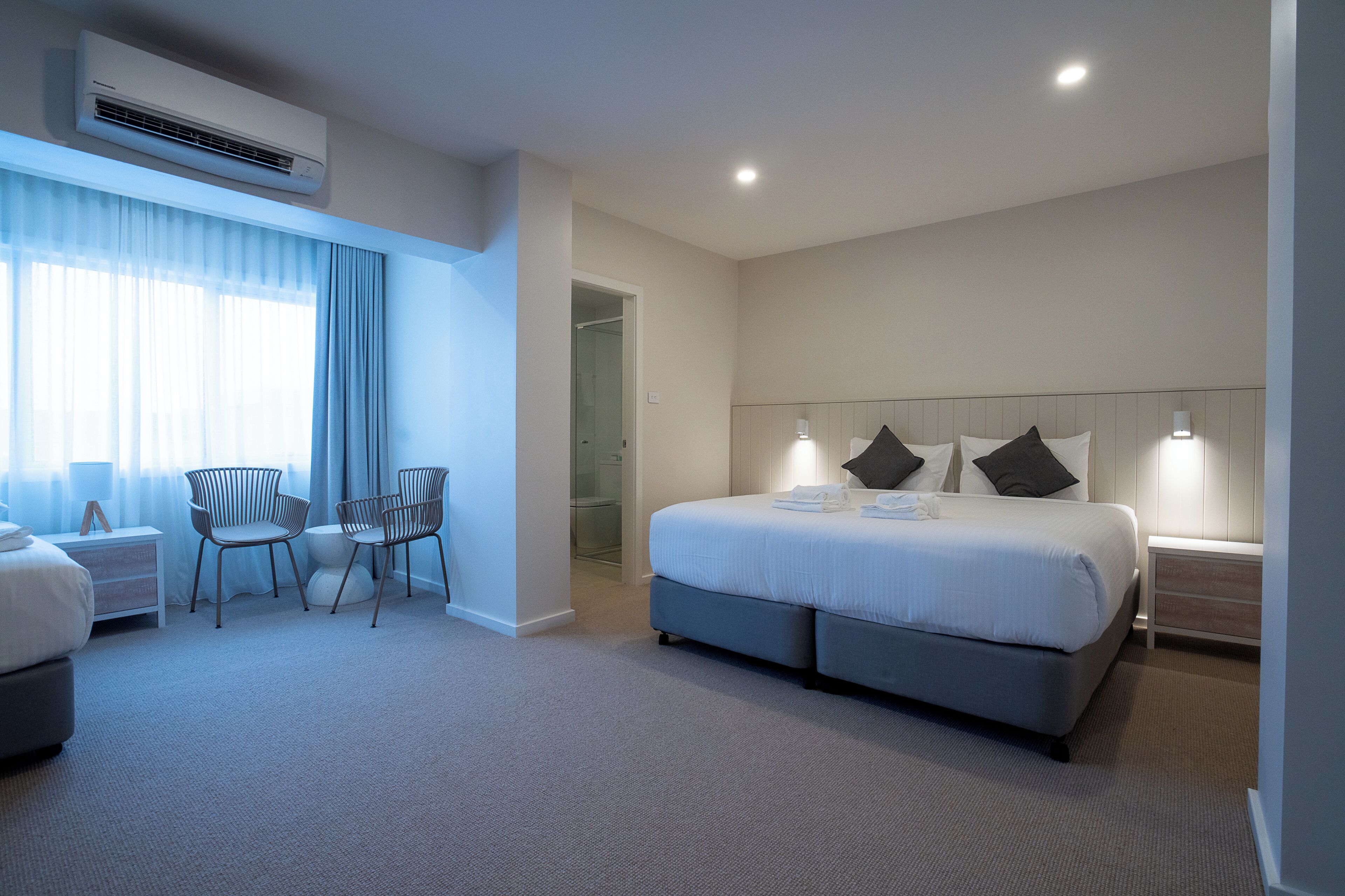 Une chambre d’hôtel moderne avec un grand lit, deux fauteuils, un bureau et un dressing.