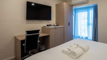 Habitación de hotel con cama, escritorio, silla, televisor y ventana con cortinas.