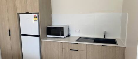 Cocina compacta con refrigerador, microondas, pileta y armarios de madera.
