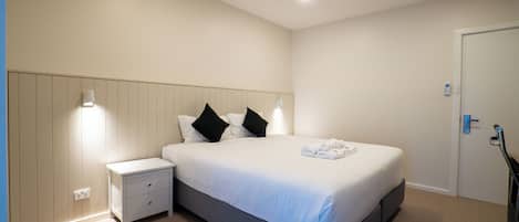Una habitación de hotel con cama, mesita de noche y una puerta.