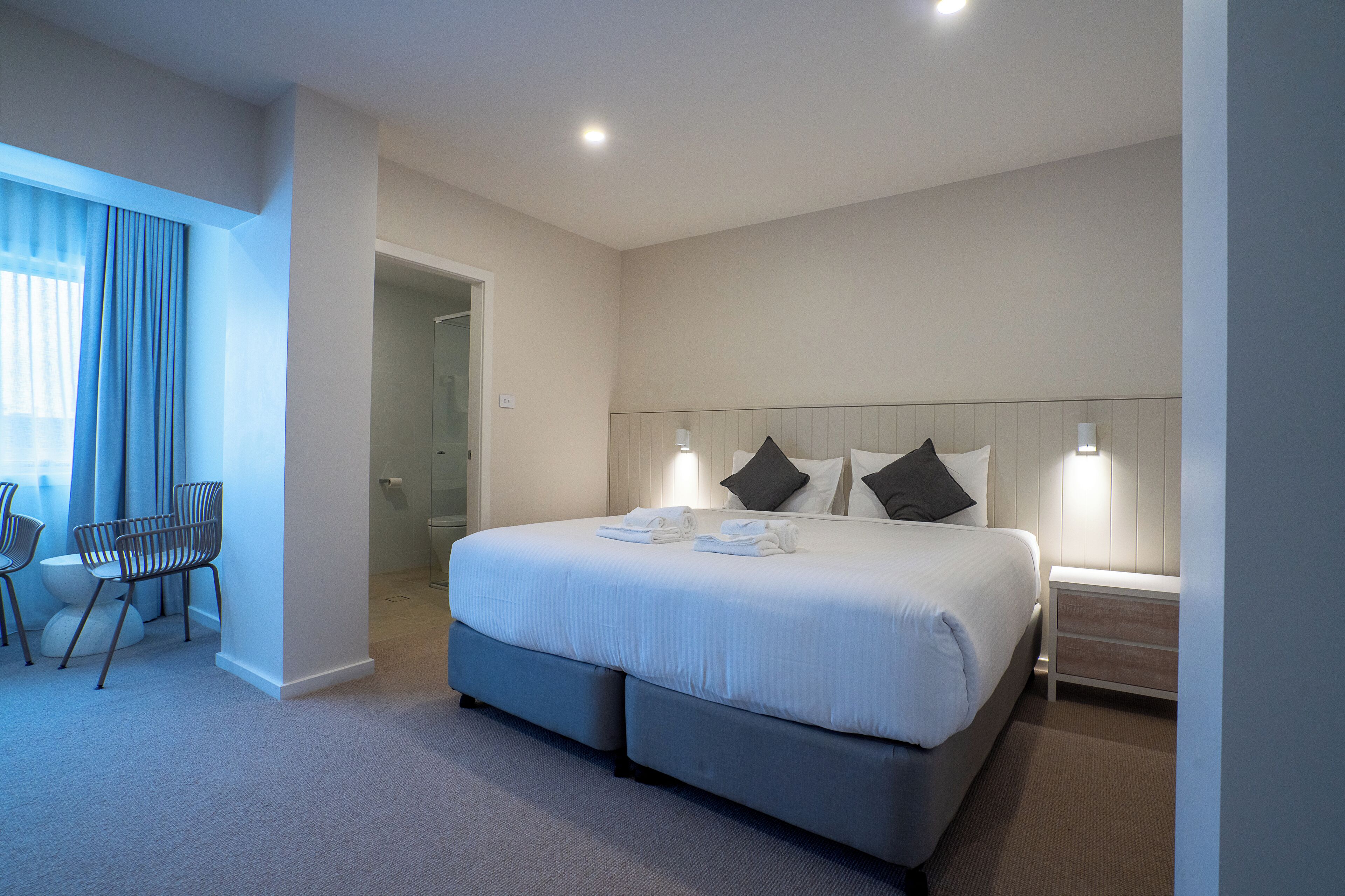 A modern hotel room with a large bed, bedside tables, a desk, and chairs.