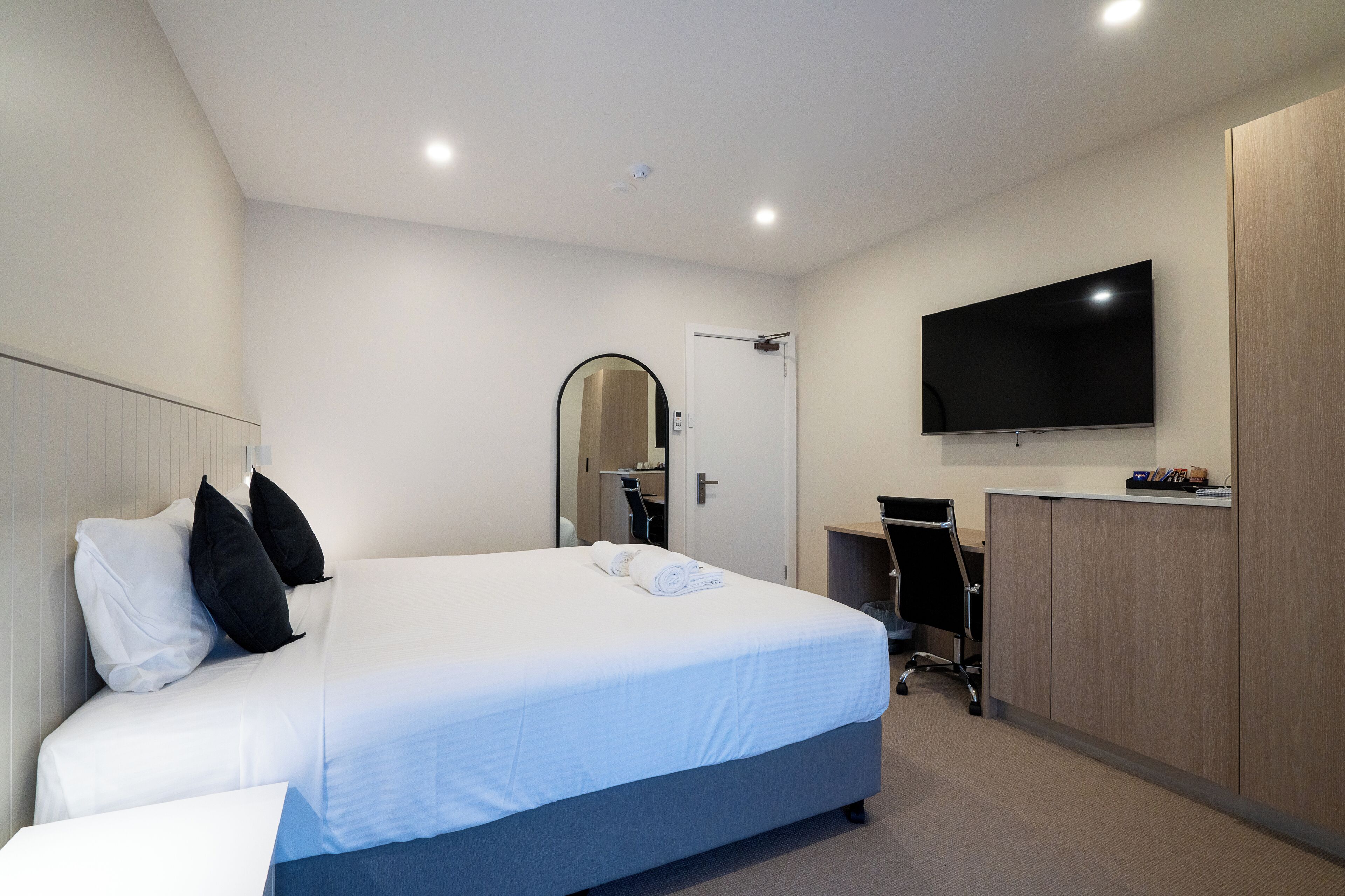 Una habitación de hotel moderna con una cama grande, un escritorio, un televisor de pantalla plana y un armario.