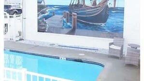 Ein Wandgemälde eines Segelschiffs an einem Steg mit einem Leuchtturm, einem Pool und einem weißen Gebäude mit Balkonen.