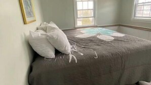 Ein Schlafzimmer mit einem Bett, zwei Fenstern, einer Deckenleuchte und einem gerahmten Bild an der Wand.