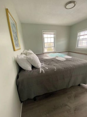 Quarto com cama, duas janelas, luminária no teto e quadro na parede.
