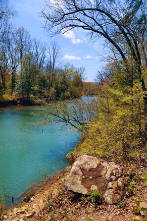 Un paysage naturel avec un lac aux eaux limpides, entouré d’arbres et dominé par un grand rocher au premier plan.