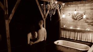 Un baño de estilo antiguo y tenuemente iluminado, con pared de madera, una bañera vintage y un candelabro.