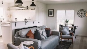 Una sala de estar moderna con un sofá gris, una mesita redonda y una zona de comedor con una silla y una mesa.
