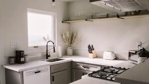 Una cocina moderna con armarios blancos, lavavajillas integrado, estufa y ventana que proporciona luz natural.
