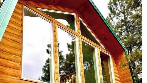 A log cabin with a steeply pitched roof, large windows, and a visible door with a decorative handle.