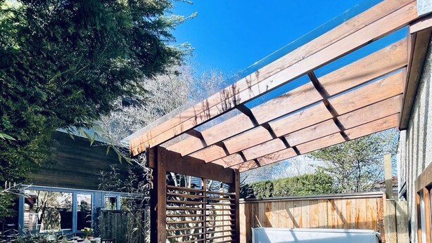 A hot tub in a wooden deck area with a pergola overhead.