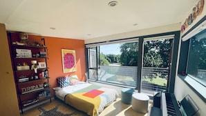 A modern bedroom with a large bed, a piano, a bookshelf, and a view of a balcony.