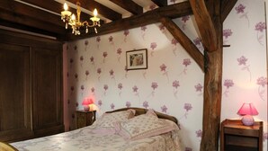 Ein Schlafzimmer mit Holzboden, Blumen-Tapete, einem Bett mit gemusterten Bettwäsche und zwei Nachttischlampen.