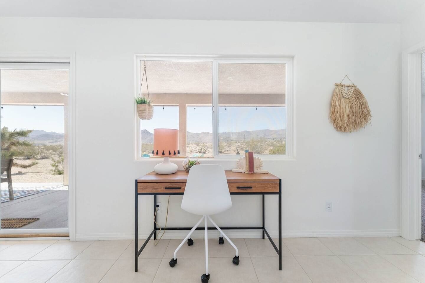 Um espaço de escritório moderno com uma mesa, cadeira e vista para uma paisagem desértica através de uma grande janela.
