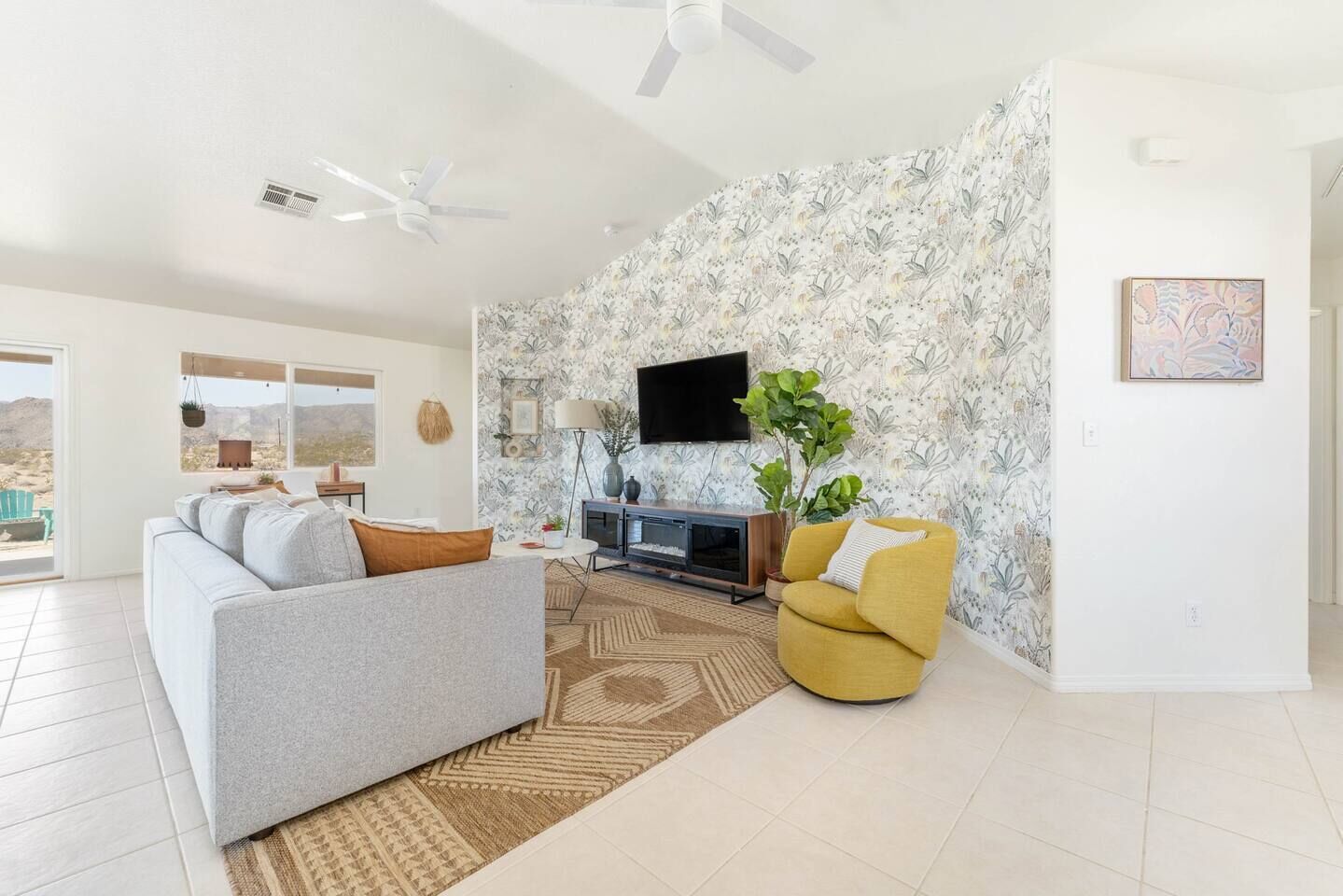 A modern living room with a grey sofa, a yellow armchair, a flat-screen TV, and a patterned wallpaper.