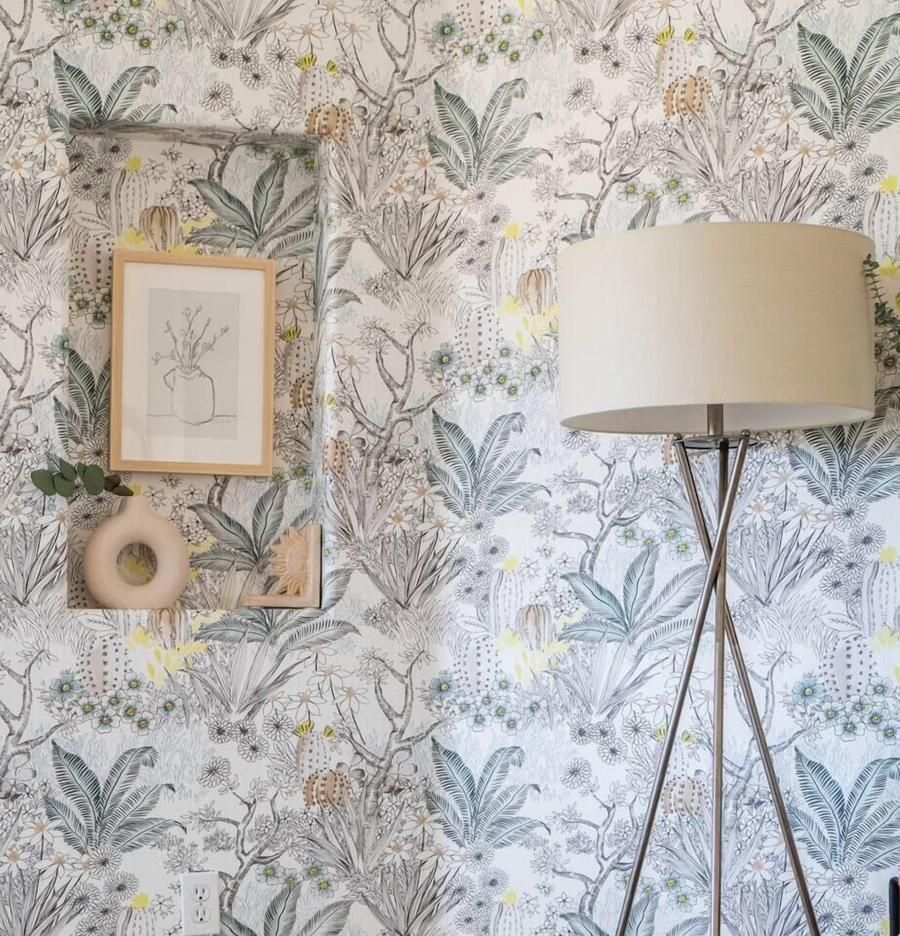 Una habitació amb paper pintat floral, una obra d'art emmarcada, un vas i una làmpada de peu.