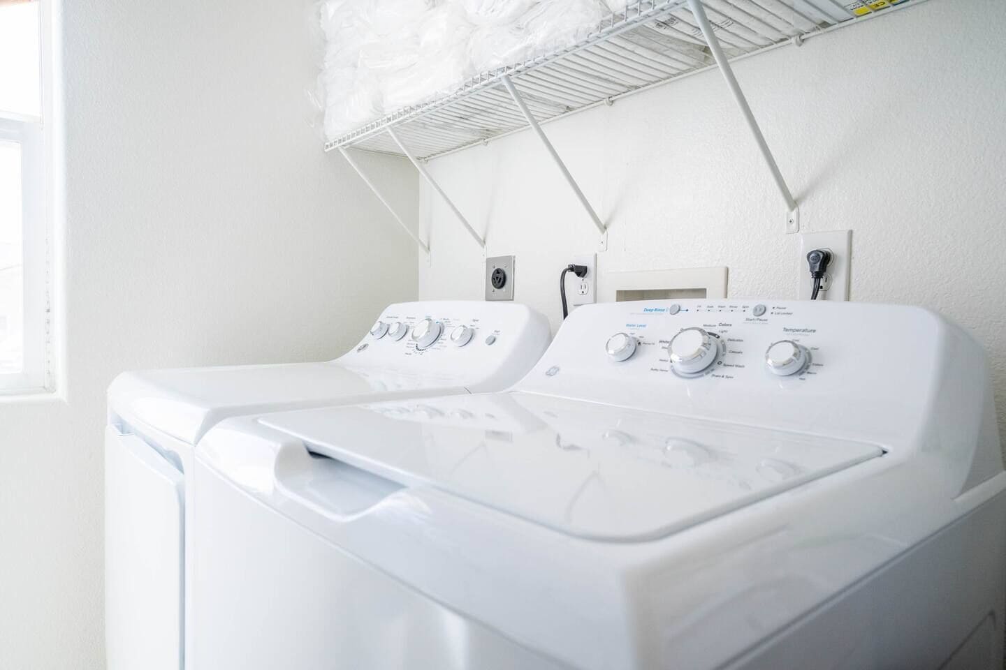 A laundry area with two front-loading washing machines and a drying rack above.