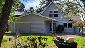 A two-story house with a garage, a front yard, and a boat in the foreground. - Very quiet Pacific City home with amazing river views from the deck! (Cloverdale)
