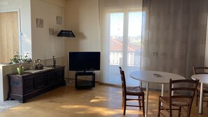 A dining area with a round table and chairs, a television on a stand, a potted plant, and a lamp. - Under The Moon: House in the Countryside Family Apartment with Balcony and Garden (Castel Bolognese)