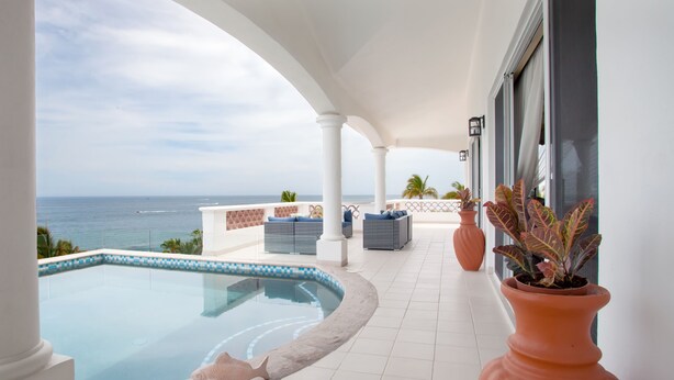 Ein Poolbereich mit Blick auf das Meer, weißen Säulen und Sitzmöglichkeiten im Freien.