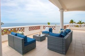 A covered outdoor seating area with wicker furniture and a view of the ocean.
