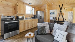 A cozy cabin interior with wooden walls, a kitchenette, a dining area, and a fireplace. - Linville Gorge 2 Bd 1 Bth Mountain Getaway! (Newland)