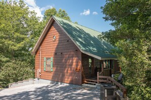A rustic cabin with a green roof, wooden exterior, and a porch with steps leading to a door. - New Listing -Couples Retreat (Sevierville)