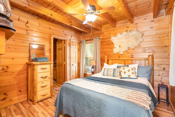 A wooden cabin bedroom with a bed, dresser, and ceiling fan. - New Listing -Couples Retreat (Sevierville)
