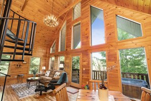 A spacious wooden cabin with a spiral staircase, large windows, a cozy living area with a sofa and coffee table, and a view of the surrounding forest. - New Listing -Couples Retreat (Sevierville)