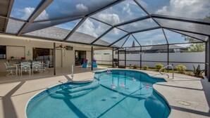 Une piscine extérieure couverte, dotée d’une structure en verre, un espace patio aménagé avec des sièges et une vue sur le ciel.