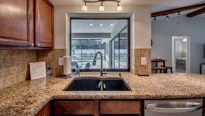 Une cuisine dotée de plans de travail en granit, d’un évier en acier inoxydable, de meubles en bois et offrant une vue sur une piscine grâce à une grande fenêtre.