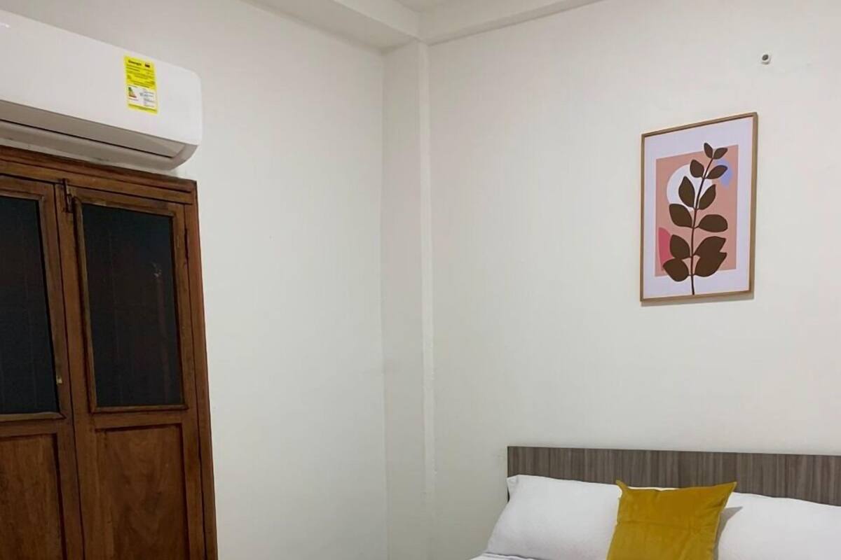 A bedroom with a bed, a wooden wardrobe, a framed picture on the wall, and a yellow blanket on the bed.
