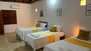 A hotel room with three beds, each with a white bedspread and a yellow runner. There is a wooden door and a wall-mounted air conditioner. - Casa Gran Fuente (Cartagena)