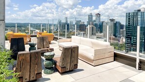 Een dakterras met moderne meubels, uitzicht op een stadshemelbeeld en een glazen balustrade.