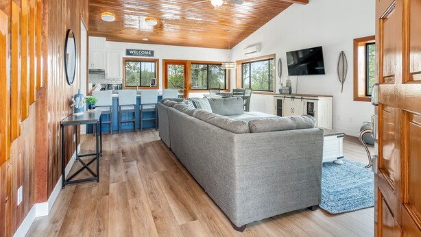 A spacious living area with a gray sectional sofa, wooden ceiling, and a kitchen area with a bar. - Bass Lake House|Boat Slip|BBQ| Fire Pit |3/2 (Bass Lake)