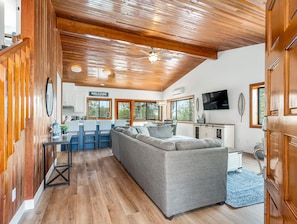 Ein geräumiger Wohnbereich mit grauem Ecksofa, Holzboden und einer Küchenzeile mit Bar.