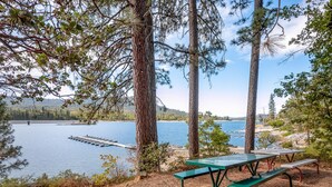 A lakeside picnic area with a table and benches, surrounded by trees and a dock extending into the water. - Bass Lake House|Boat Slip|BBQ| Fire Pit |3/2 (Bass Lake)