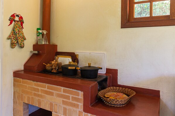 Una cocina con horno de ladrillo, ollas, una cesta y una ventana.