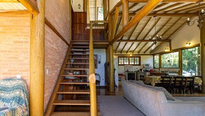 Una escalera de madera conduce a un altillo con una mesa de comedor y sillas, un sofá y una cocina con ventana que da a zonas verdes.