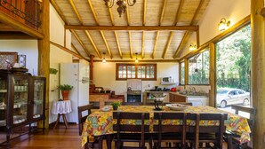 Un área de comedor con una mesa y sillas de madera, una cocina al fondo y vistas al exterior.
