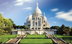 A large, white domed building with multiple towers, surrounded by a well-maintained lawn and a stone bridge leading to it.
