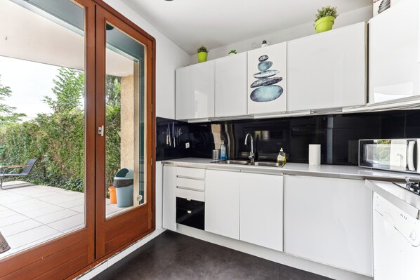 A modern kitchen with white cabinets, a microwave, and a sink. There are two potted plants on the cabinets.