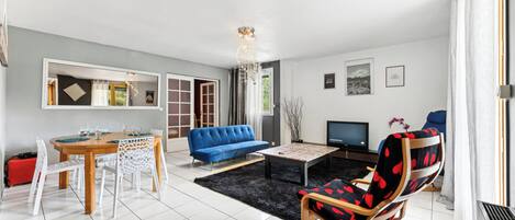 A modern living room with a blue sofa, a dining table with chairs, a coffee table, and a TV.