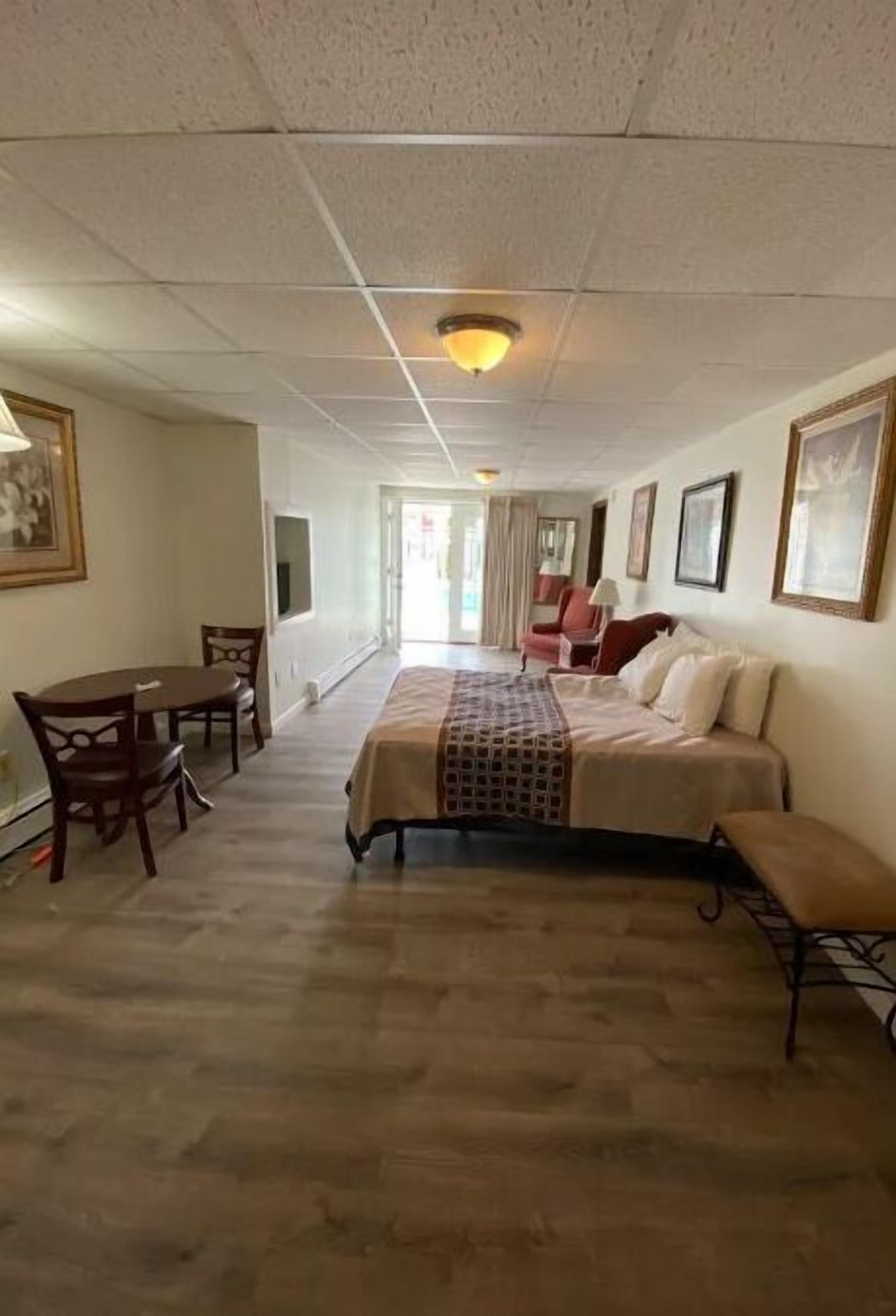 A hotel room with a bed, a desk, and chairs. There is a hallway leading to another room.